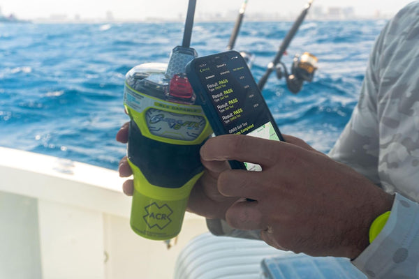 User holding ACR GlobalFix V6 EPIRB with smartphone app for GPS testing and emergency readiness