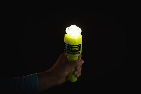 Hand holding ACR ResQFlare electronic distress flare glowing brightly in dark for emergency signaling