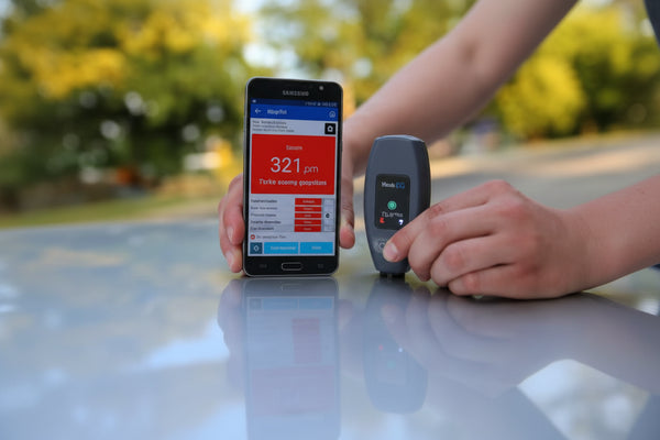 Wireless NexPTG paint thickness gauge with Bluetooth app displaying coating thickness results